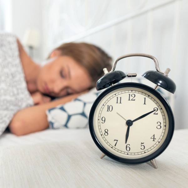 Image of an alarm clock next to someone sleeping.