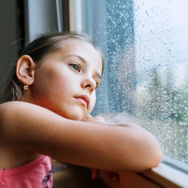 child looking longingly into a window with rain droplets