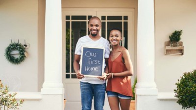 Couple holding up a “Our first home” sign in front of their new home