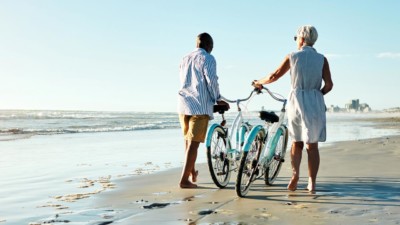Older couple walking their bikes along the beach