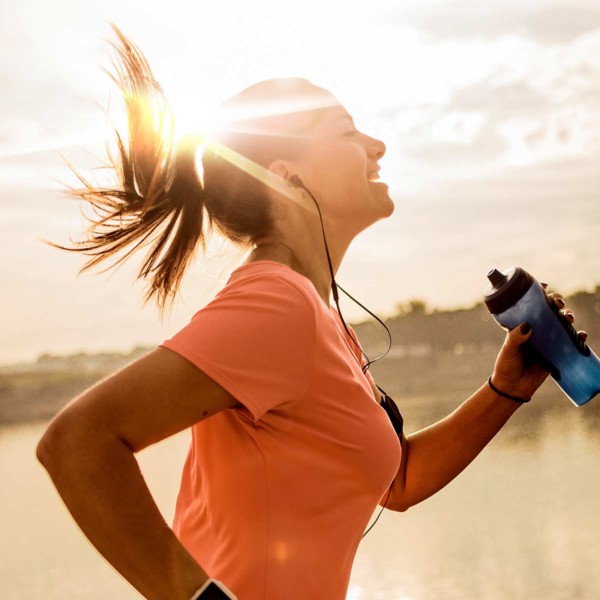 Image of a person running with a bottle of water with the sun in the background.