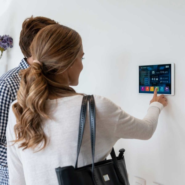 Image of people using a tablet with smart home controls mounted to a wall.